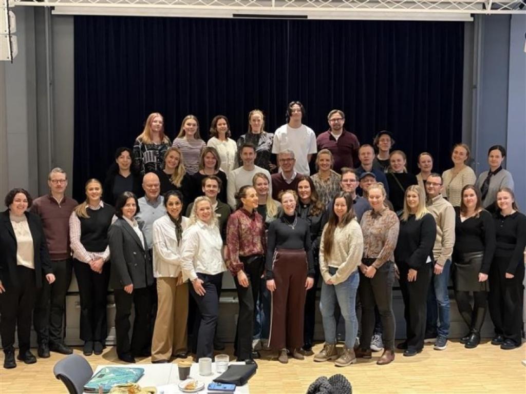 Stor gruppe deltakere samlet foran en scene, poserer for fellesbilde.