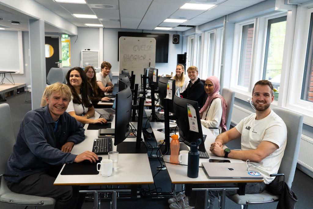 DigdirCamperne sitter rundt bordet med dataskjermer og smiler til kamera.