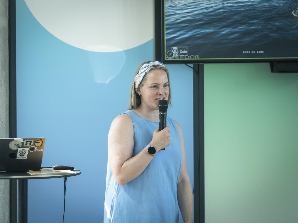 Thea Pope avbildet på scenen med mikrofon i hånden mens hun ser ut på publikum
